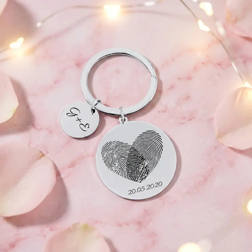 Personalisierter Schlüsselanhänger aus Edelstahl mit Fingerabdruck-Gravur in Herzform und Datum auf rosa Hintergrund.