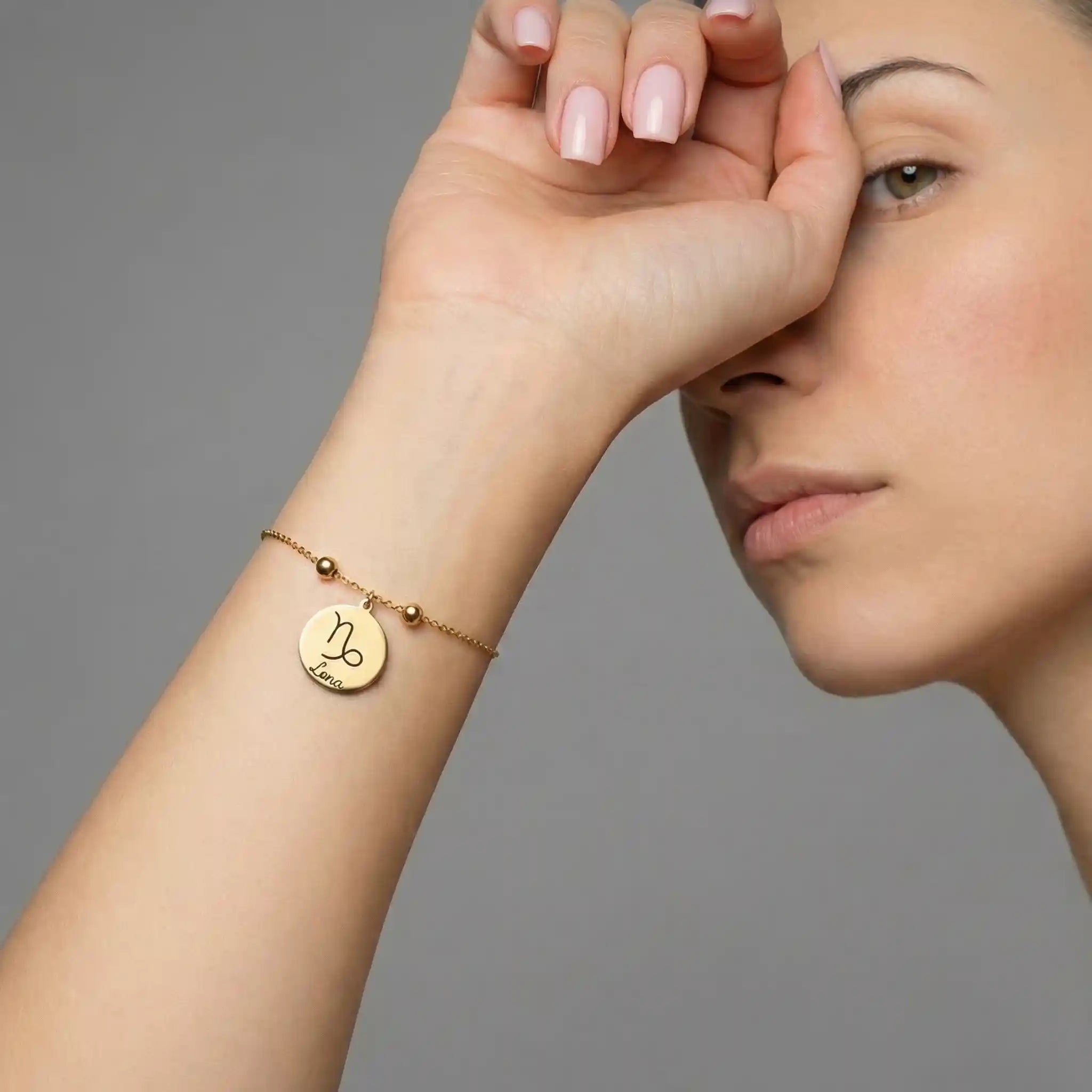 Frau trägt ein goldfarbenes Edelstahlarmband mit rundem Anhänger, graviert mit einem Sternzeichen und Namen, elegantes und personalisiertes Schmuckdesign.