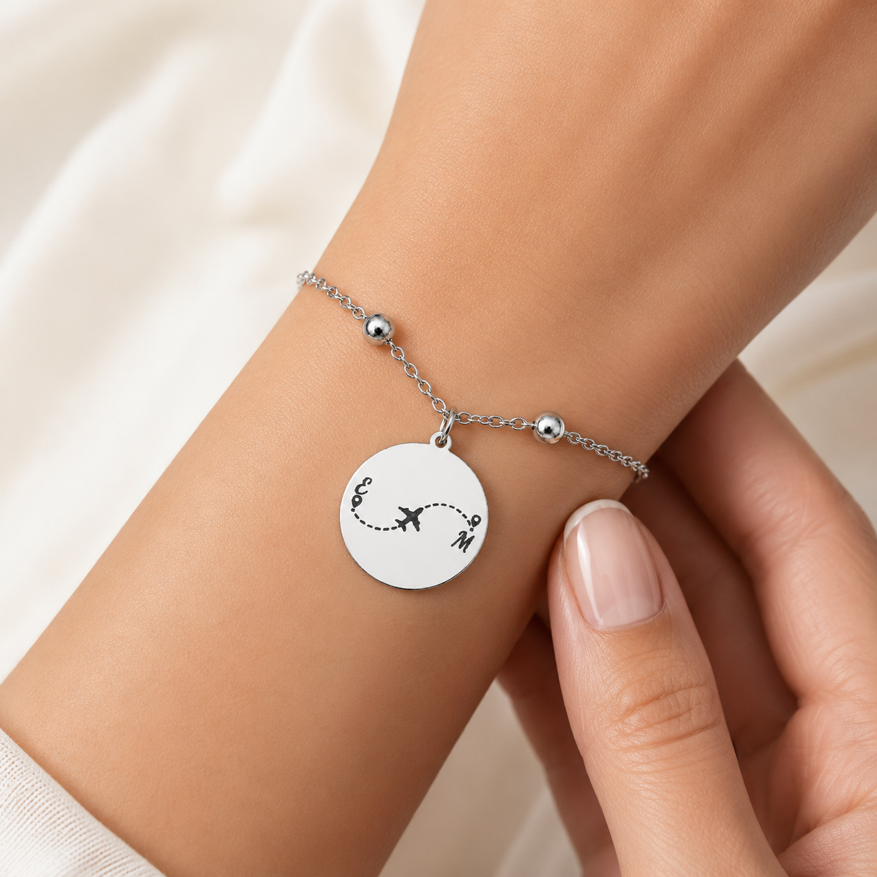 Silbernes personalisiertes Edelstahl Armband mit rundem Anhänger, Gravur eines Flugzeugs mit gepunkteter Route zwischen zwei Initialen, am Handgelenk getragen
