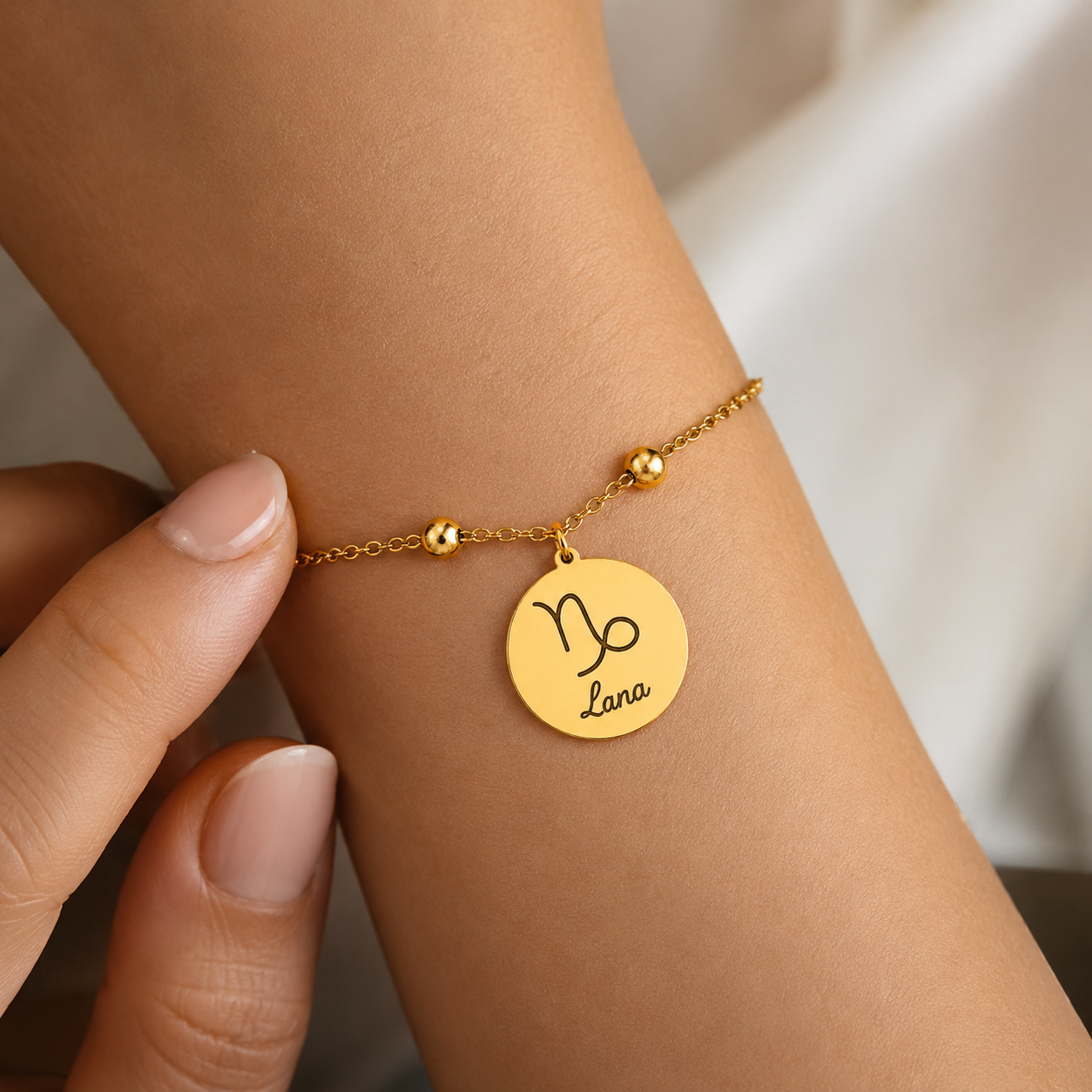 Goldenes personalisiertes Edelstahl Armband mit rundem Anhänger, Sternzeichen Steinbock und Gravur „Lana“, am Handgelenk getragen