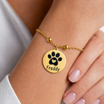 Goldenes personalisiertes Edelstahl Armband am Handgelenk getragen, mit rundem Anhänger, Pfotenmotiv mit Herz und Name Freddy