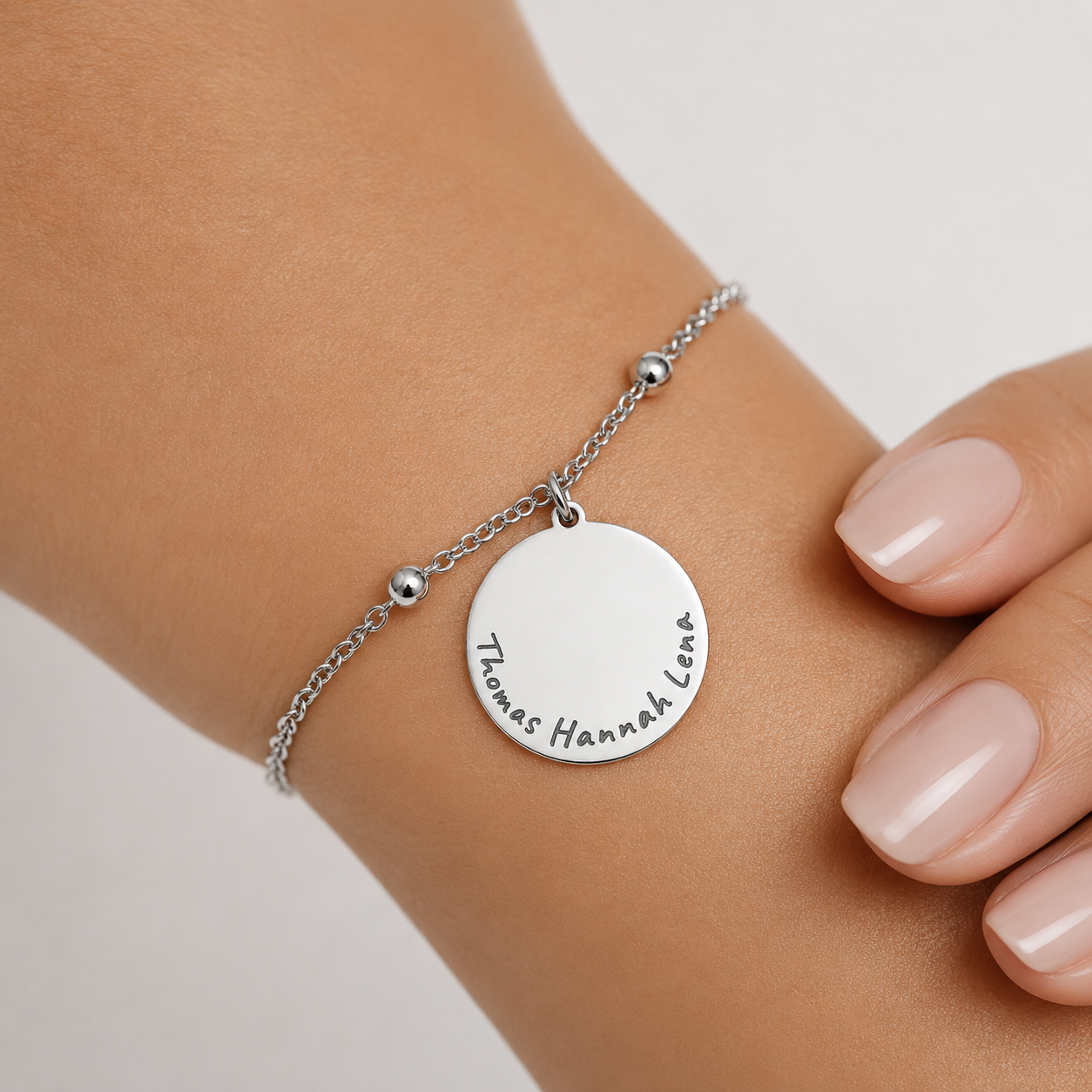 Silbernes personalisiertes Edelstahl Armband mit rundem Anhänger und Gravur „Thomas Hannah Lena“, am Handgelenk getragen