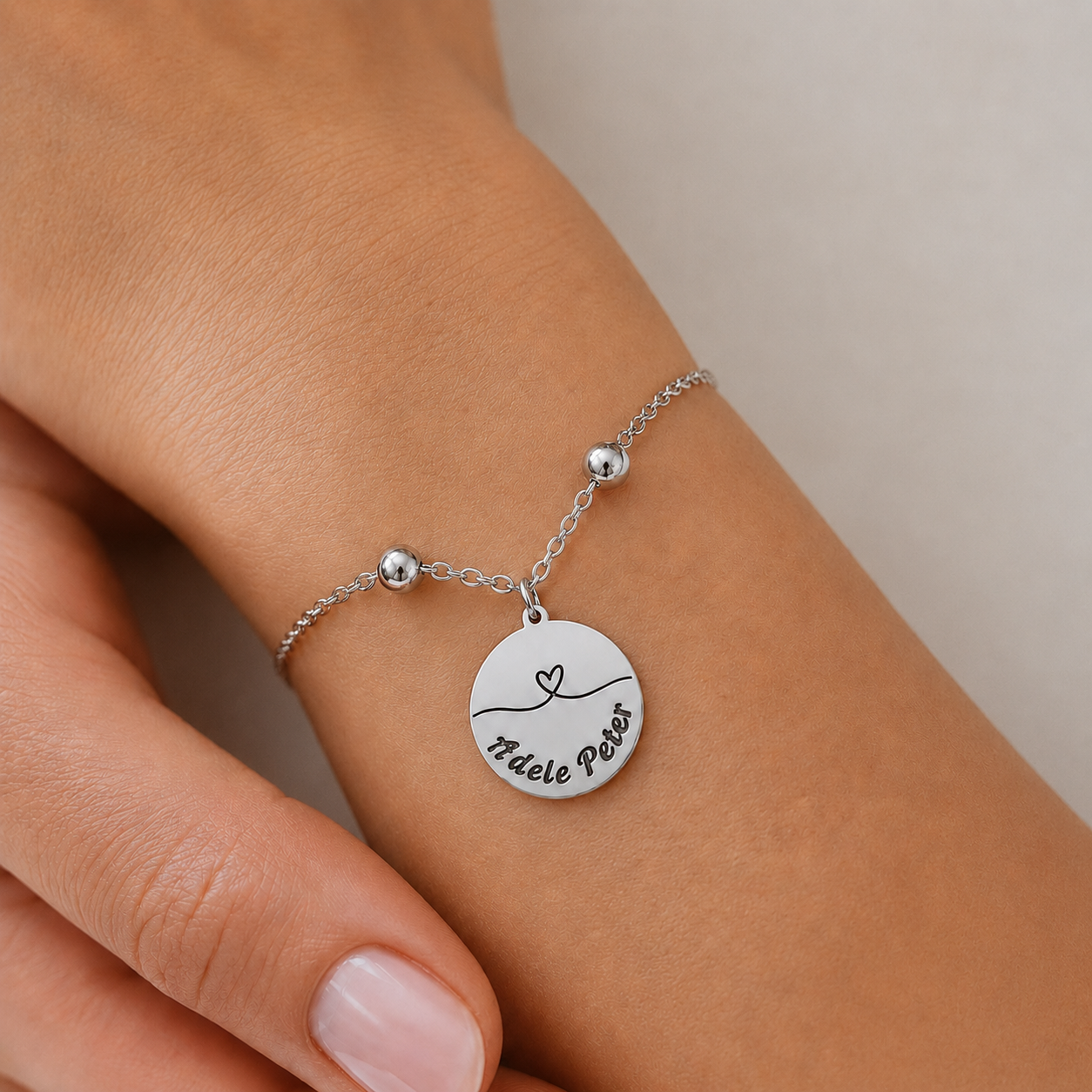 Silbernes personalisiertes Edelstahl Armband mit rundem Anhänger, Herzlinie Motiv und Gravur „Adele Peter“, am Handgelenk getragen
