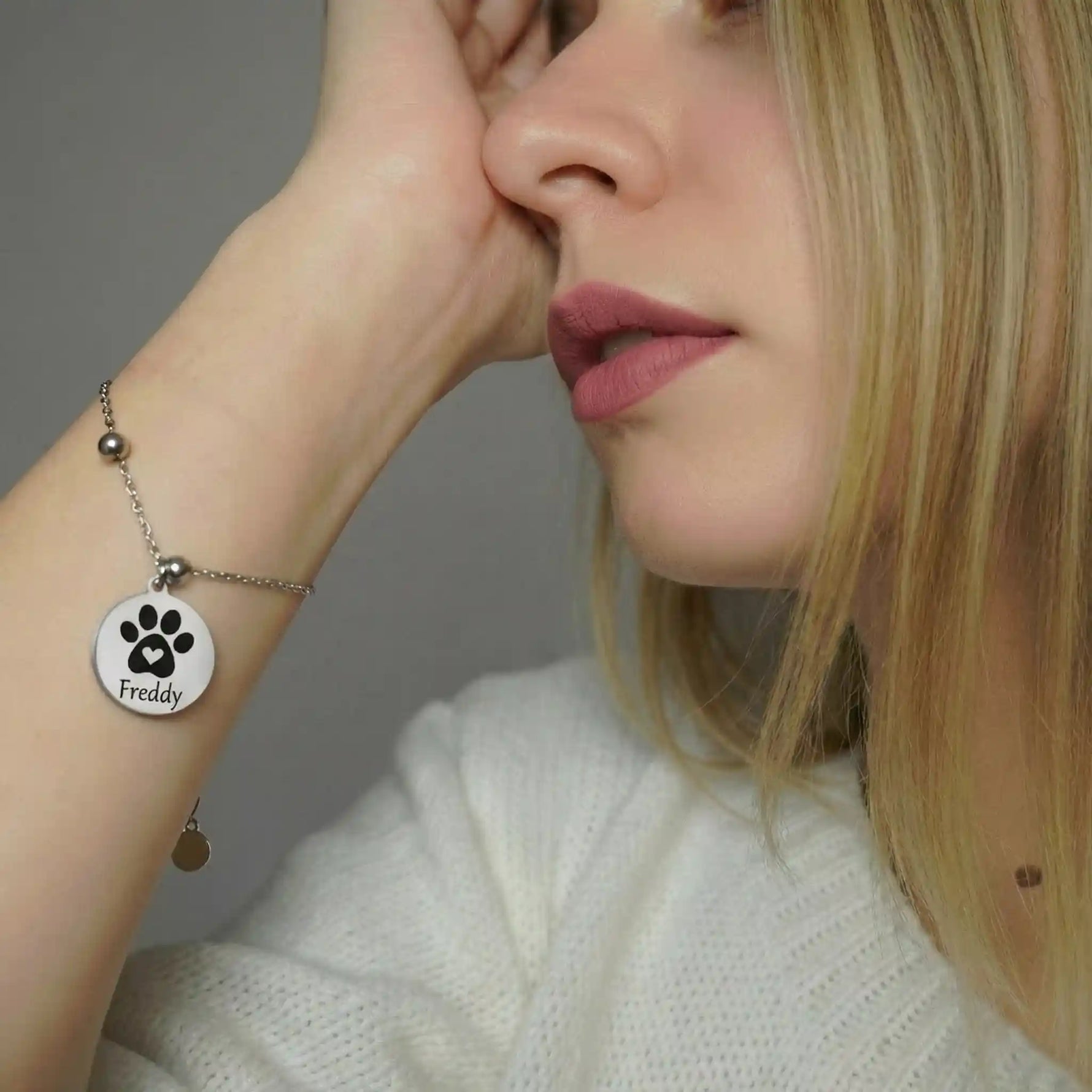 Frau trägt ein silberfarbenes Edelstahlarmband mit rundem Anhänger, graviert mit einer Pfote und dem Namen „Freddy“, personalisiertes Tierarmband für Hund oder Katze.