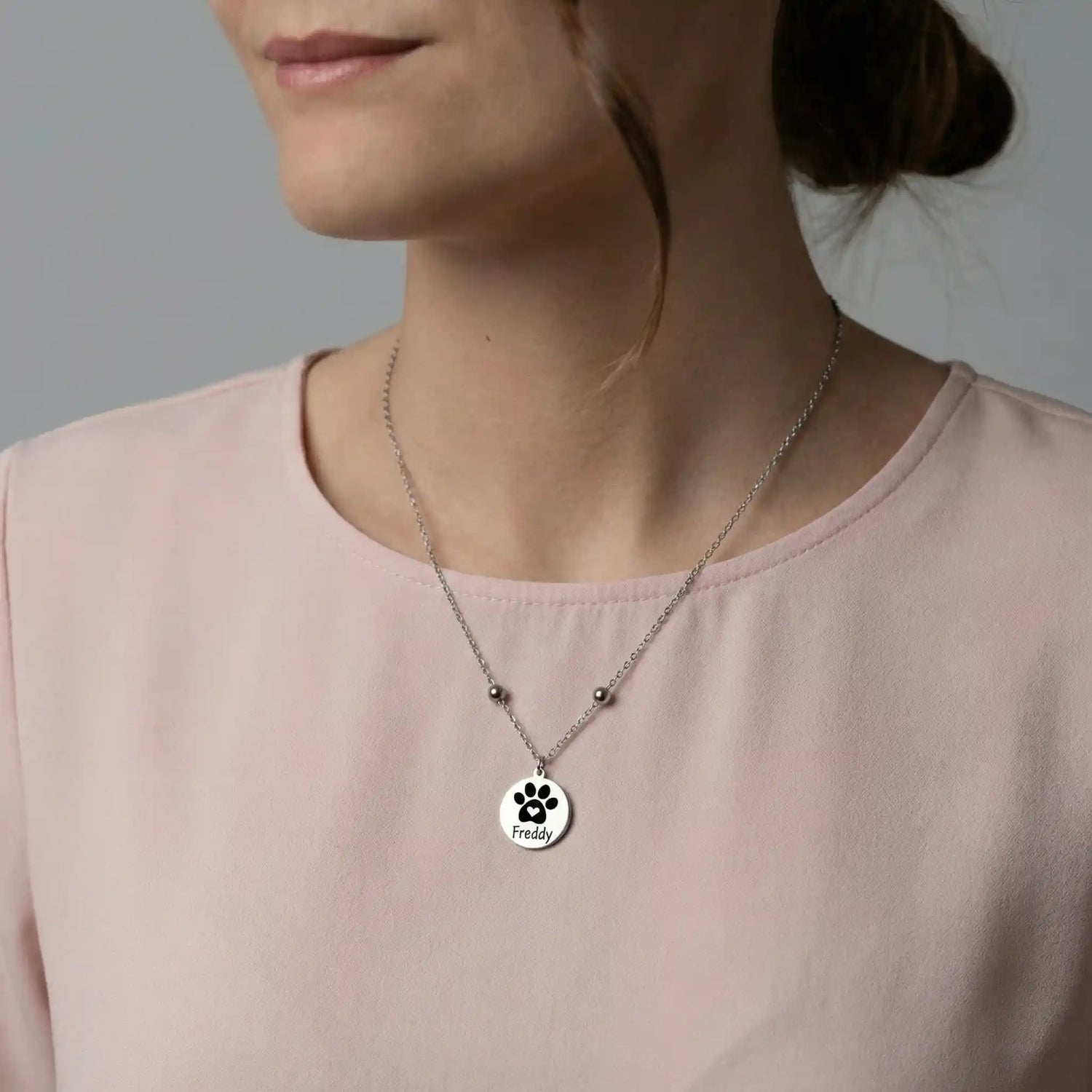 Frau trägt eine silberfarbene Edelstahlkette mit rundem Anhänger, graviert mit einer Pfote und einem Namen, personalisierte Tierhalskette mit schlichtem Design.