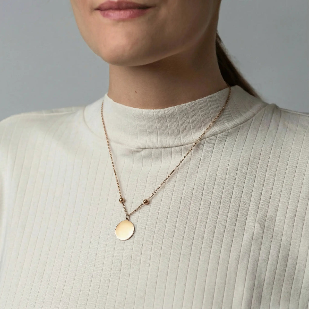 Frau trägt eine goldfarbene Edelstahlkette mit rundem, glattem Anhänger und verstellbaren Stoppern, individuell gravierbar.