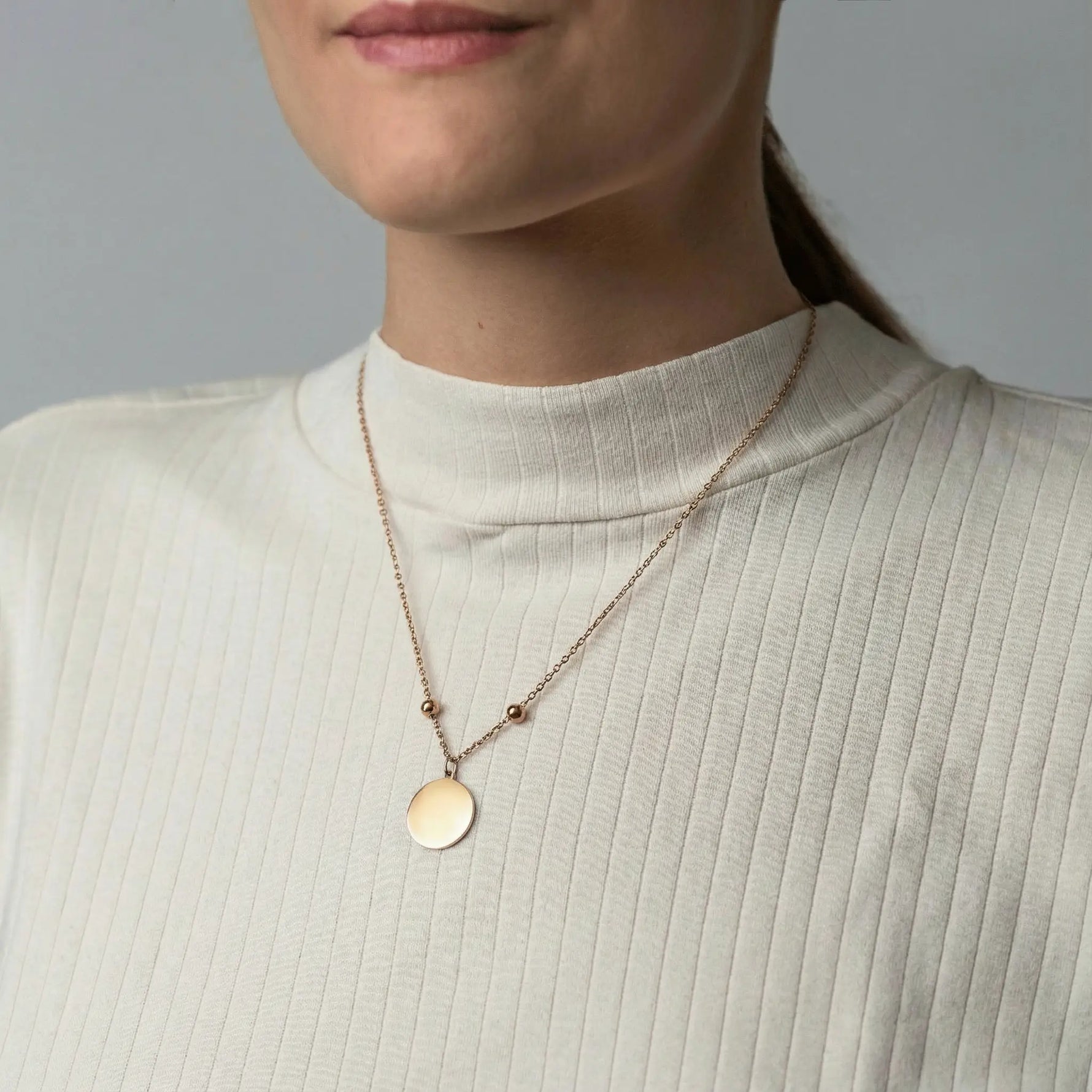 Frau trägt eine goldfarbene Edelstahlkette mit rundem, glattem Anhänger und verstellbaren Stoppern, individuell gravierbar.