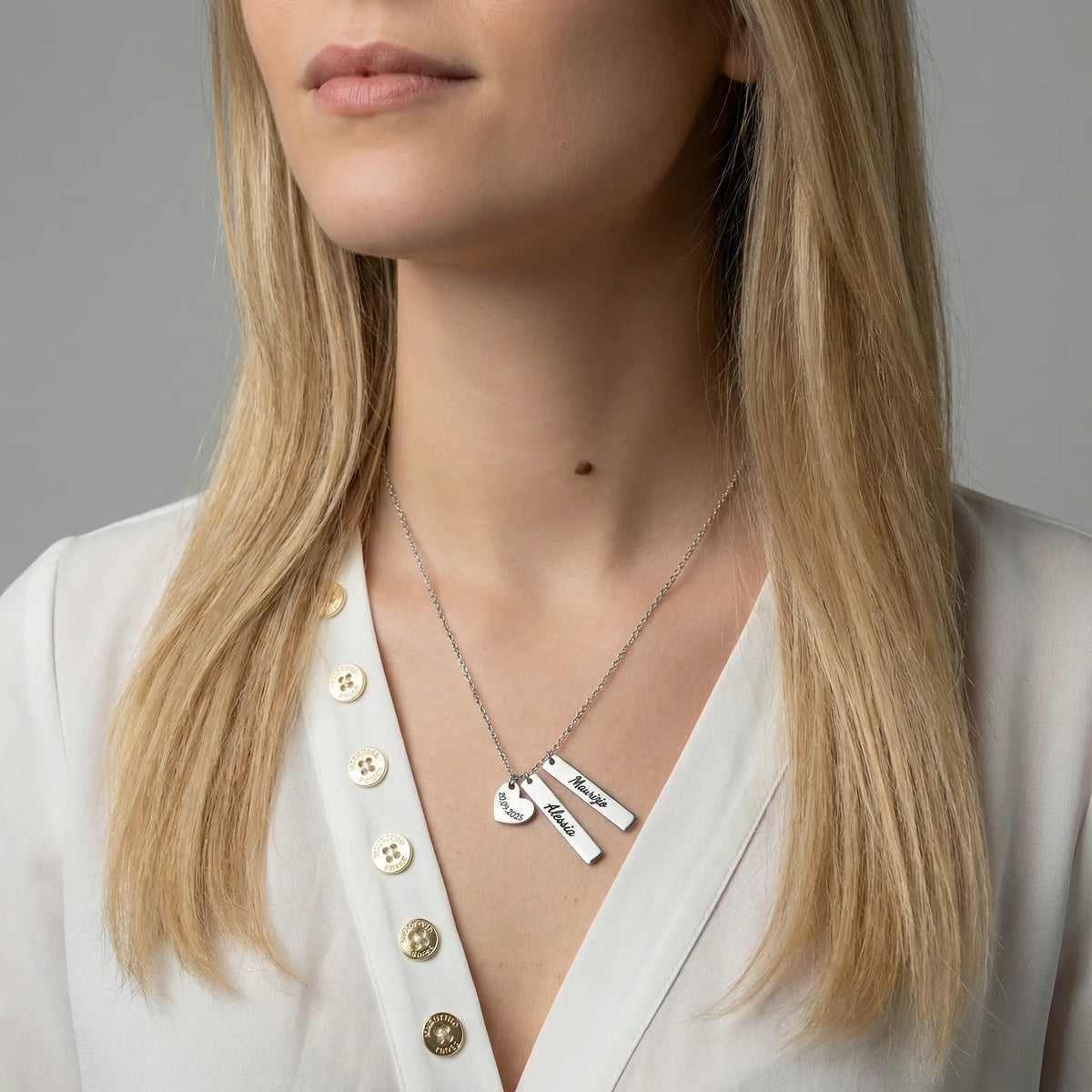 Frau trägt eine silberfarbene Edelstahlkette mit mehreren schmalen, personalisierten Anhängern, graviert mit Namen und Datum, elegantes und zeitloses Design.