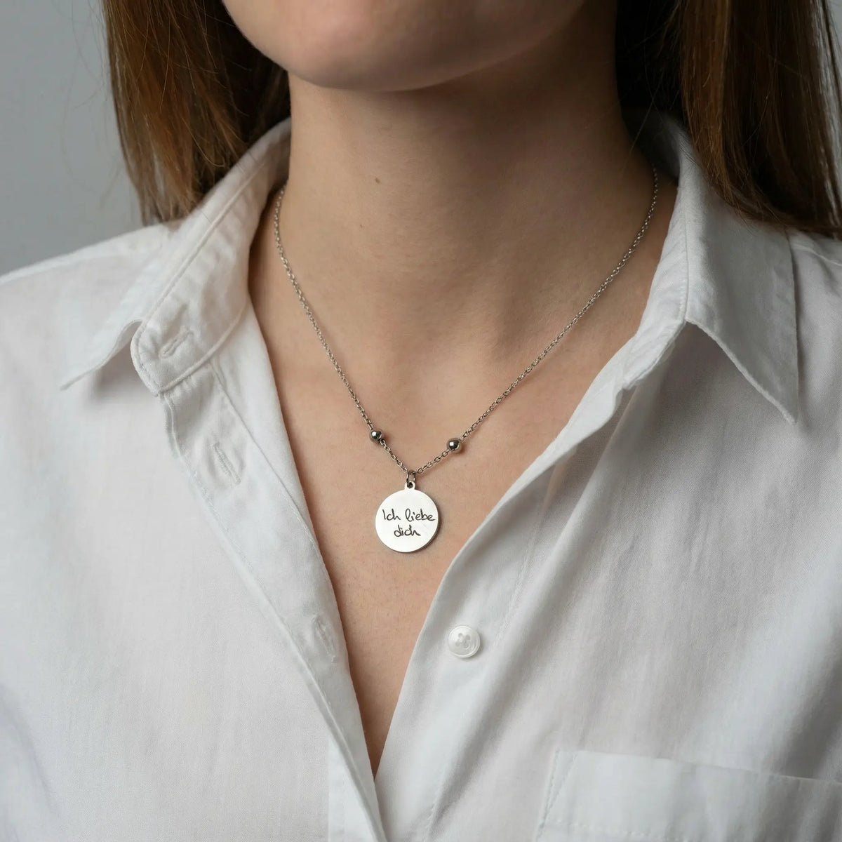 Frau trägt eine silberfarbene Edelstahlkette mit rundem Anhänger und gravierter Botschaft am Hals.