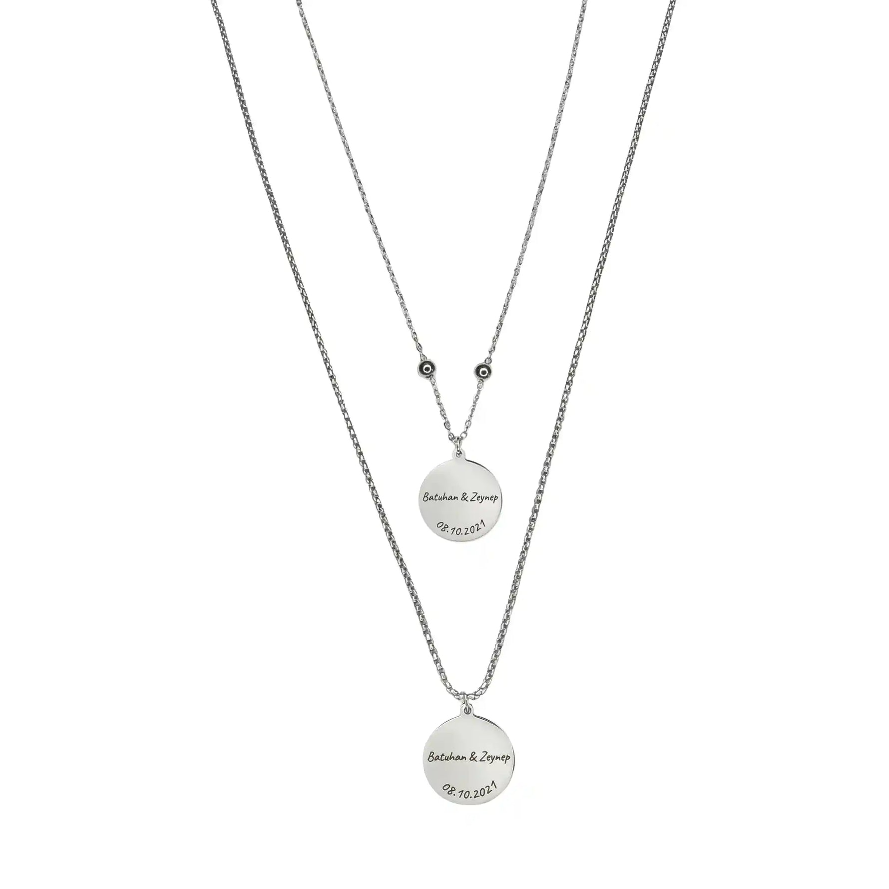 Zwei silberfarbene Edelstahl-Partnerhalsketten mit runden Anhängern, personalisiert mit Namen und Datum, minimalistisches Schmuckdesign.