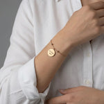 Frau trägt ein goldfarbenes, personalisiertes Edelstahlarmband mit rundem Anhänger und gravierter Botschaft am Handgelenk.